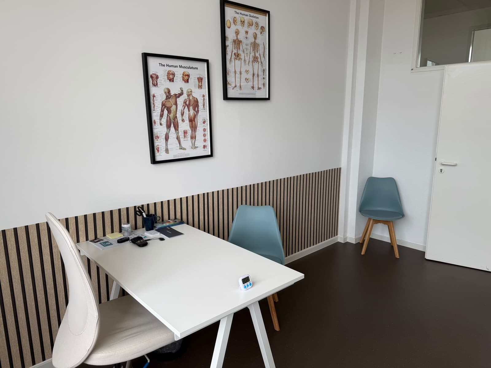Befundraum mit Schreibtisch, Stühlen und Anatomie-Postern an der Wand